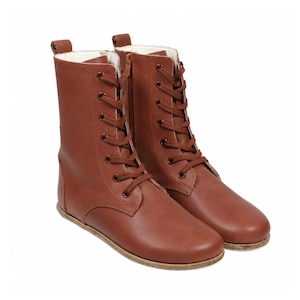 May include: A pair of mid-calf boots in a solid brown color featuring a lace-up front with matching brown laces, metal eyelets, a side zipper closure, a pull tab at the heel, and a light-colored interior lining with a flat sole.