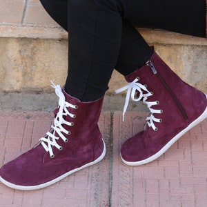 May include: Burgundy suede ankle boots with white laces and a zipper on the side. The boots have a white rubber sole.