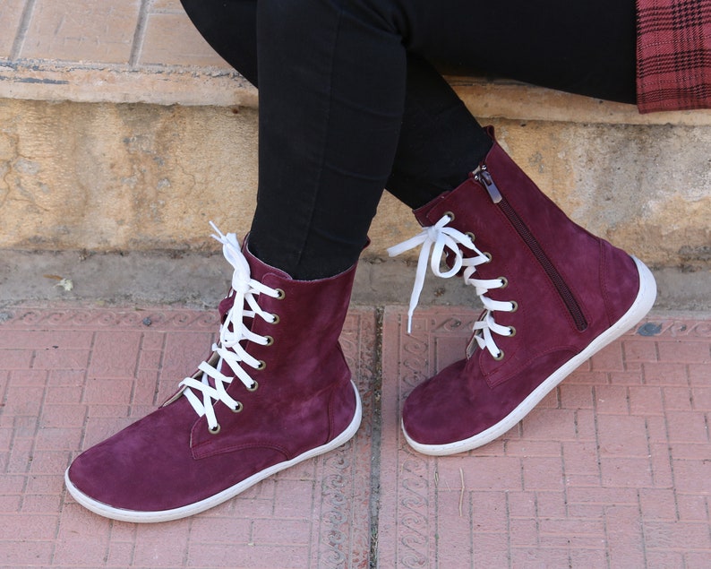 May include: Burgundy suede ankle boots with white laces and a zipper on the side. The boots have a white rubber sole.