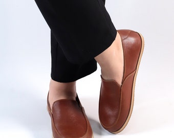 May include: A pair of brown leather slip-on shoes with a slightly rounded toe. The shoes have a simple design and a comfortable look.