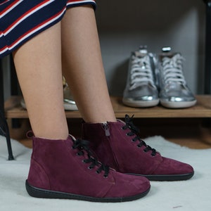 May include: A pair of burgundy suede high-top sneakers with black laces and a zipper on the side. The sneakers have a black rubber sole.