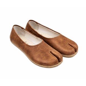 May include: A pair of brown leather split-toe ballet flats. The shoes have a rounded toe box and a split design for the big toe. The soles are a light tan color. The shoes are designed for comfort and style.