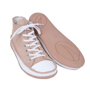 May include: Beige high-top sneakers with white laces and a white rubber sole. The shoes have a furry texture and are made of leather.