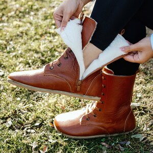 May include: Brown leather boots with a white fur lining. The boots have laces and a zip on the side.