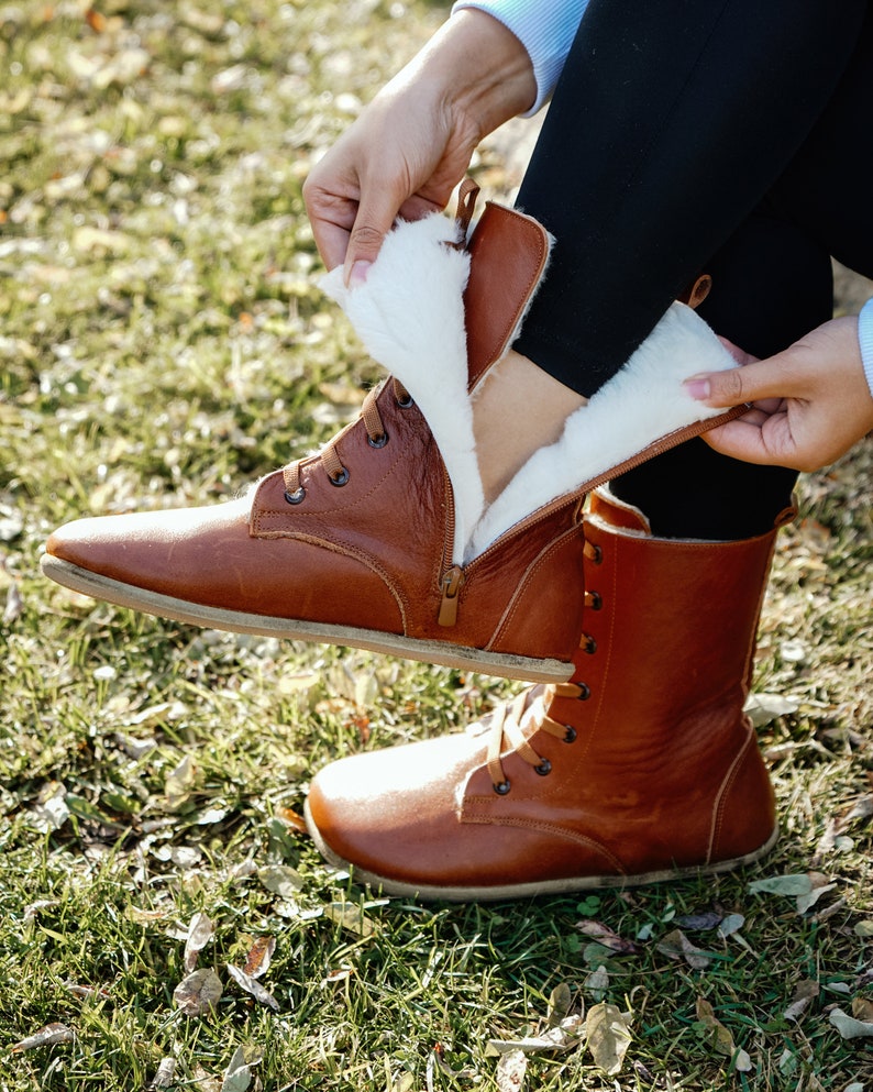 May include: Brown leather boots with a white fur lining. The boots have laces and a zip on the side.