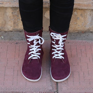 May include: Burgundy suede boots with white laces. The boots have a rounded toe and a low heel.