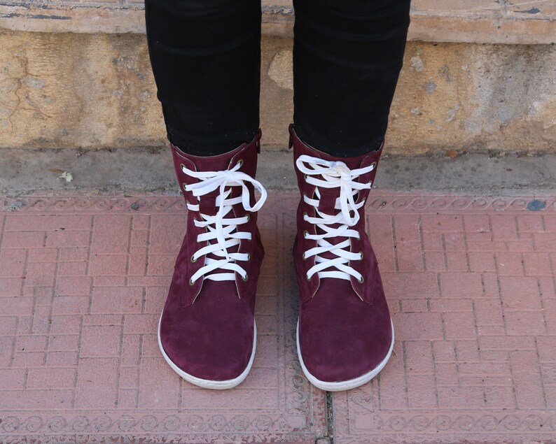 May include: Burgundy suede boots with white laces. The boots have a rounded toe and a low heel.