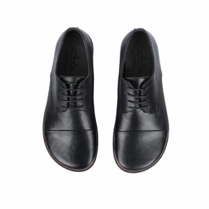 May include: A pair of black leather dress shoes with a lace-up design. The shoes have a rounded toe and a smooth, polished finish. The soles are a dark brown color. The shoes are designed for formal occasions.