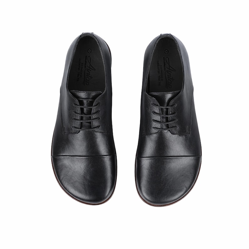 May include: A pair of black leather dress shoes with a lace-up design. The shoes have a rounded toe and a smooth, polished finish. The soles are a dark brown color. The shoes are designed for formal occasions.