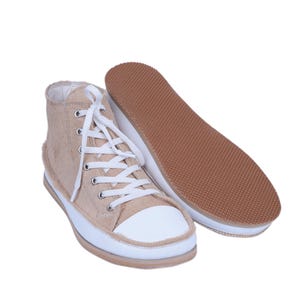 May include: Beige high-top sneakers with white laces and a white rubber toe cap. The sneakers have a brown rubber outsole.