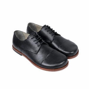 May include: A pair of black leather dress shoes with a rounded toe and a brown sole. The shoes have black laces and a classic, formal design. The shoes are displayed on a white background.