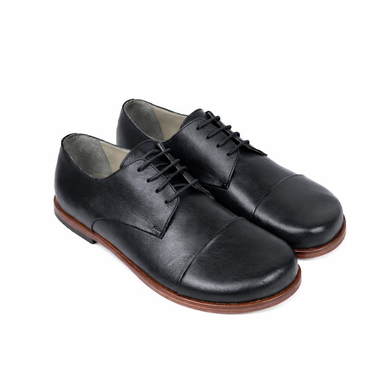 May include: A pair of black leather dress shoes with a rounded toe and a brown sole. The shoes have black laces and a classic, formal design. The shoes are displayed on a white background.