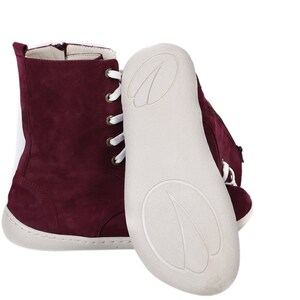May include: Burgundy suede ankle boots with white laces and a white rubber sole. The boots have a zipper on the inside of the ankle.