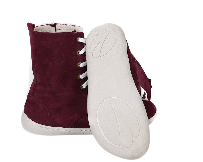 May include: Burgundy suede ankle boots with white laces and a white rubber sole. The boots have a zipper on the inside of the ankle.