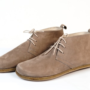 May include: A pair of light brown suede ankle boots with laces. The boots have a flat sole and a rounded toe.