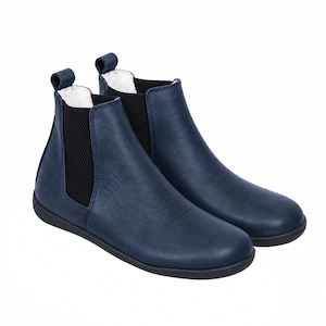 May include: A pair of navy blue Chelsea boots featuring a smooth finish, black elastic side panels, and a pull tab at the heel. The boots have a rounded toe, a low-profile black sole, and a white interior lining visible at the top opening.