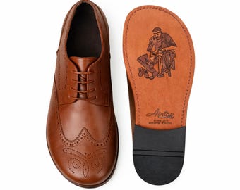 May include: A brown leather brogue shoe with decorative perforations and laces. The insole, displayed separately, features a shoemaker illustration and the brand name "Aintap". The shoe is shown next to its insole.