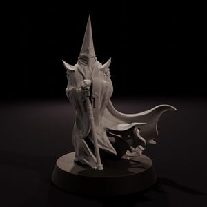 May include: A detailed, off-white figurine of a robed figure with a tall, pointed hood. The figure holds a staff with a cross and skull design. The figure is standing on a circular base, with a long cape flowing behind it.