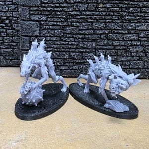May include: Two gray, 3D-printed fantasy miniatures of skeletal wolf-like creatures. One holds a spiked ball, the other stands with a skeletal paw. Both are on black oval bases, set against a textured dark gray brick wall.