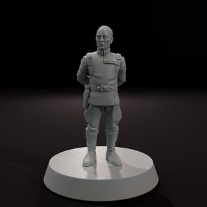 May include: A gray figurine of a man in a military-style uniform, standing on a circular base. The uniform includes a high-collared jacket, pants, and boots. The figure has his hands behind his back.