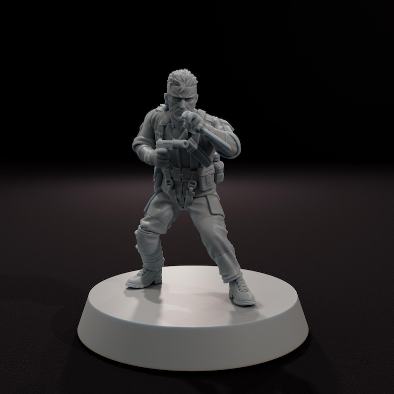 以下が含まれることがあります： 銃とナイフを持った戦闘服姿の兵士の灰色のフィギュア。フィギュアは、暗い背景に対して、白い円形の台座の上に立っています。兵士はブーツ、ズボン、ベスト、長袖シャツを着ています。