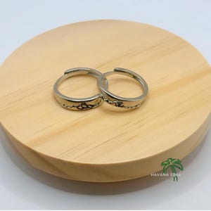 Op de afbeelding: Twee zilveren ringen met een berg- en golfontwerp. De ringen liggen op een licht houten oppervlak.