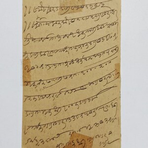 Puede incluir: Un trozo rectangular de papel envejecido con texto manuscrito en tinta negra. El papel tiene un tono marr&oacute;n claro y est&aacute; ligeramente rasgado en los bordes. La escritura parece estar en un idioma extranjero.