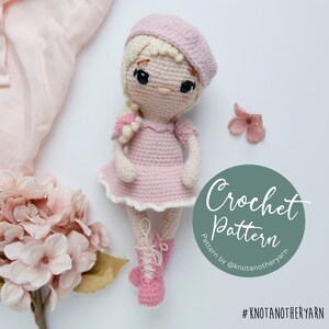 May include: Crochet pattern for a pink doll with blonde hair, wearing a pink dress and a pink beret. The doll is sitting on a white background with pink flowers. The pattern is by @knotanotheryarn and the hashtag is #knotanotheryarn.