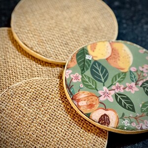 May include: Four round coasters, three are a natural burlap material and one is a green, floral design with peach and yellow fruit.