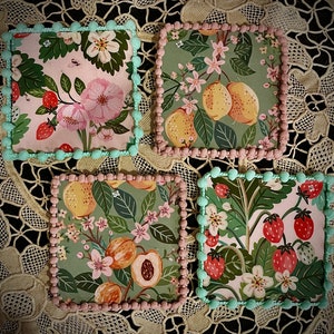 May include: Four square ceramic coasters with floral and fruit designs. The coasters feature a variety of colors, including pink, green, yellow, and blue. The designs are intricate and detailed, and the coasters are perfect for adding a touch of elegance to any home.