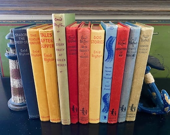 Könnte beinhalten: Eine Sammlung alter Enid Blyton-Bücher mit Titeln wie "Dog Stories" und "The Tales After Supper". Die Bücher haben farbige Buchrücken und sind in einer Reihe angeordnet. Das Bild zeigt das klassische Design und die gealterten Einbände.