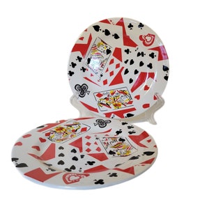 May include: Two white ceramic plates with a red, black, and white design of playing cards and spades. The plates are stacked on top of each other.