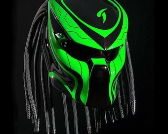 May include: A black and green motorcycle helmet with a Predator-inspired design. The helmet has a black visor and a green face mask. The helmet has a long, black braid hanging from the back.