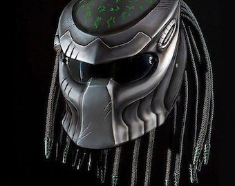 Può includere: Un casco da moto argentato con un design a dreadlock nero e verde. Il casco ha una visiera trasparente e uno schermo verde con un motivo.