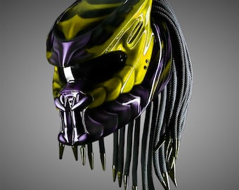 May include: A yellow and purple motorcycle helmet with a black dreadlock-style design. The helmet has a predator-like face mask with sharp teeth.