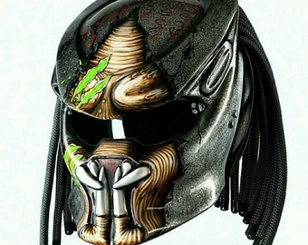 May include: A silver and brown motorcycle helmet with a Predator design. The helmet has a black visor and black dreadlocks.