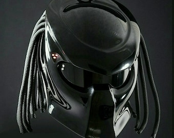 May include: A black motorcycle helmet with a Predator-inspired design. The helmet has a black visor and a black and gray braided strap.