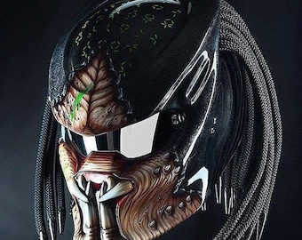 May include: Black motorcycle helmet with a Predator-inspired design. The helmet has a black and brown paint scheme with a detailed Predator face and dreadlocks.