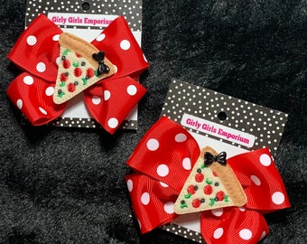 Könnte beinhalten: Zwei rote Haarschleifen mit Polka-Dots und einem Pizzastück-Design. Jede Schleife hat eine schwarze Schleifenverzierung und ist an einer schwarz-weiß gepunkteten Karte mit dem Text "Girly Girls Emporium" befestigt.