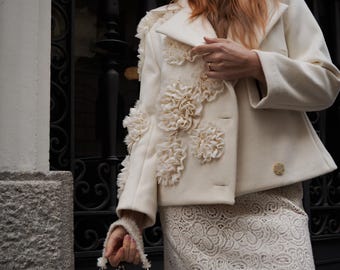 May include: A white coat with a floral design on the sleeve, a white lace skirt, and a white handbag with a pearl embellishment.