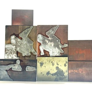 Op de afbeelding: Een set van vijf vintage houten drukblokken met metalen platen die verschillende scènes voorstellen. De blokken zijn in verschillende bruintinten en hebben een versleten, rustieke uitstraling.