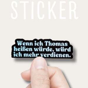 Può includere: Un adesivo nero con il testo "Wenn ich Thomas heißen würde, würd ich mehr verdienen." in azzurro. La parola "STICKER" è scritta in bianco sopra l'adesivo.