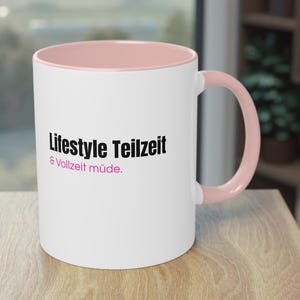 Könnte beinhalten: Weißer Keramikbecher mit rosa Innenraum und Henkel. Der Becher trägt den schwarzen Text "Lifestyle Teilzeit & Vollzeit müde". Der Becher steht auf einer Holzoberfläche.
