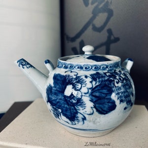 May include: A small, white teapot with a blue and white floral design. The teapot is sitting on a book with the title "Twenty Love Poems" visible.