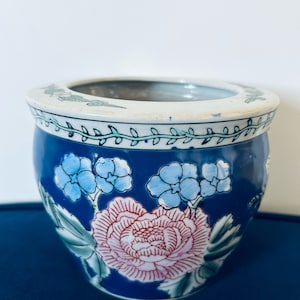 May include: A blue and white ceramic planter with a floral design. The planter features pink, blue, and green flowers on a dark blue background.