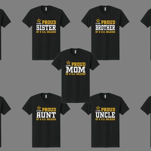 以下が含まれることがあります： 白と金色の文字がプリントされた黒いTシャツ。 「PROUD DAD」、「PROUD SISTER」、「PROUD BROTHER」、「PROUD GRANDMA」、「PROUD MOM」、「PROUD GRANDPA」、「PROUD AUNT」、「PROUD UNCLE」、および「PROUD COUSIN」の文字がプリントされています。アメリカの兵士の。