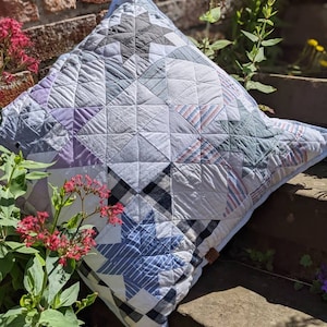 May include: A patchwork pillow with a blue, white, and black star pattern. The pillow is made from different fabrics and has a rustic, handmade look.