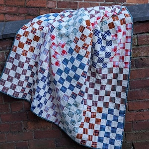 May include: A patchwork quilt with a checkered pattern in shades of blue, red, and brown. The quilt is made of different fabrics and has a white background.