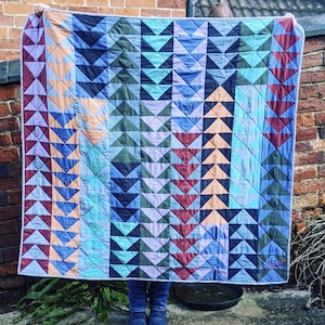 May include: A colorful quilt with a geometric pattern of triangles in shades of blue, green, red, and orange. The quilt is made of fabric scraps and has a patchwork design.