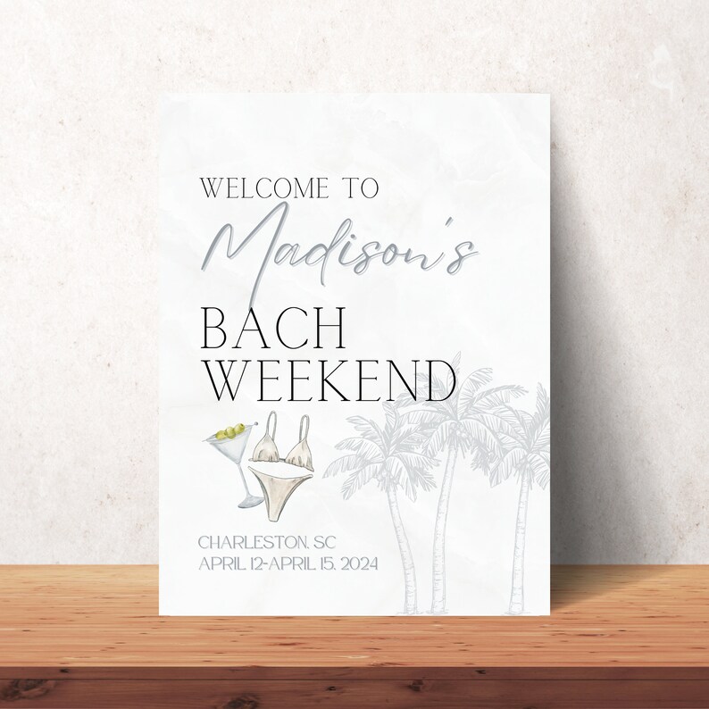 May include: A white sign with black text that says "Welcome to Madison's Bach Weekend" with a drawing of palm trees and a martini glass with olives. The text at the bottom says "Charleston, SC April 12-April 15, 2024".